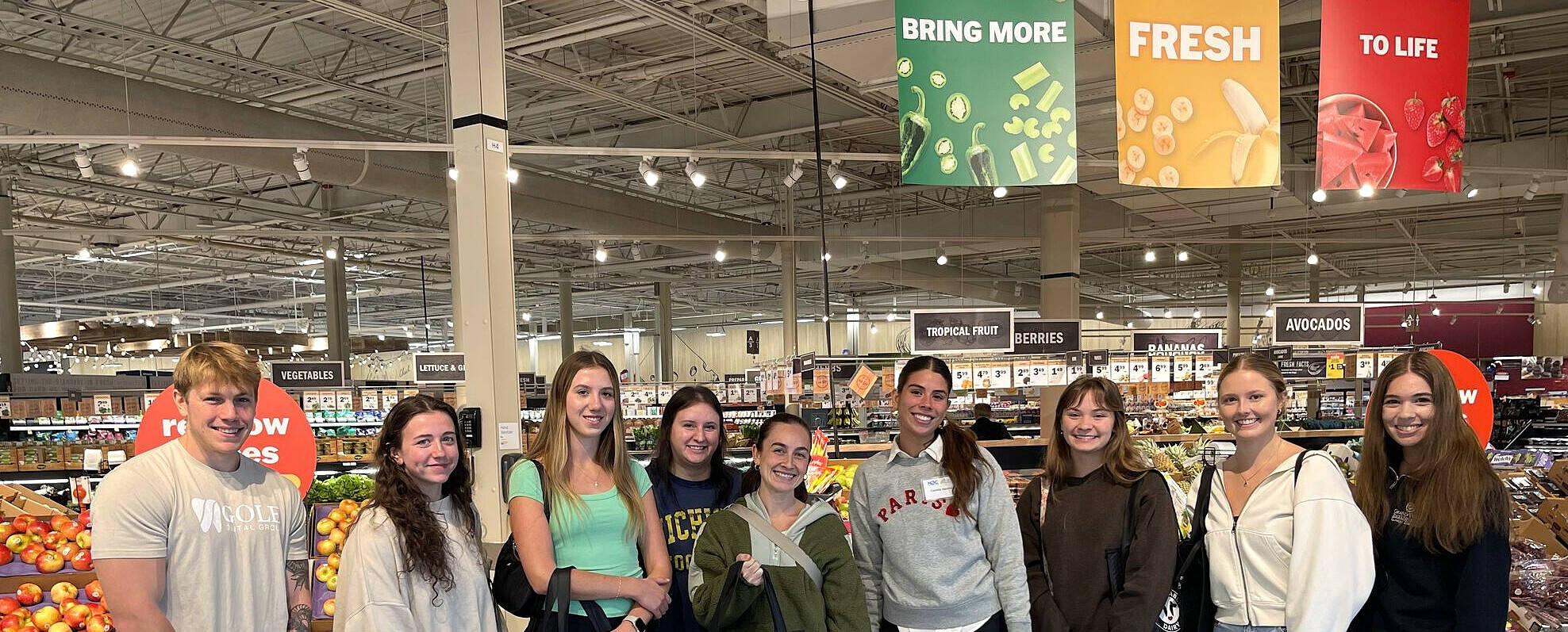 Applied Food and Nutrition students pose in a store's produce section as they prepare to shop for ingredients to be used in the Culinary Kitchen lab.